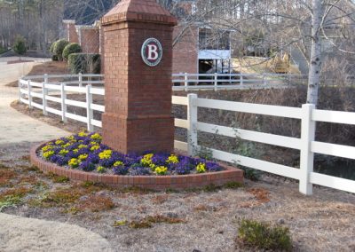 Plain white fencing along the road by a tuffet of flowers