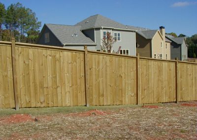 A brown wood fence for a big house on the other side