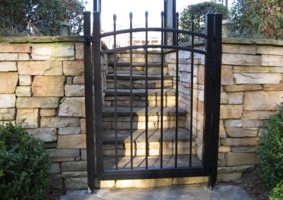 A metal gate attached to stone walls and stairs